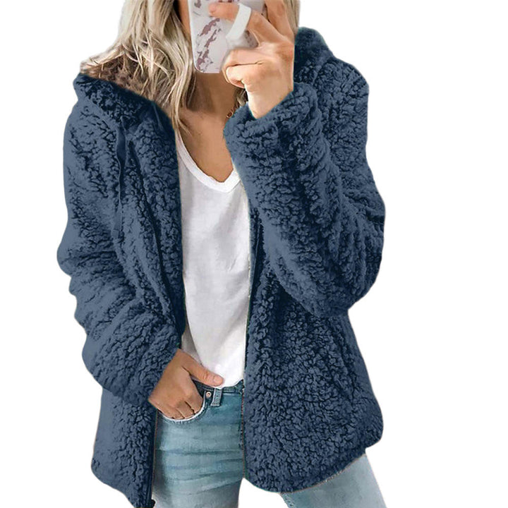 Eine Frau trägt einen blauen Pelzmantel mit Tasche und Reißverschluss, eine Hand auf der Tasche auf weißem Hintergrund